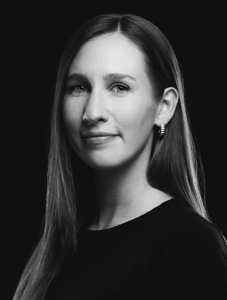 A black-and-white portrait of Jessica Sulikowski, Ballet Idaho Academy Director, with long hair and hoop earrings against a dark background.