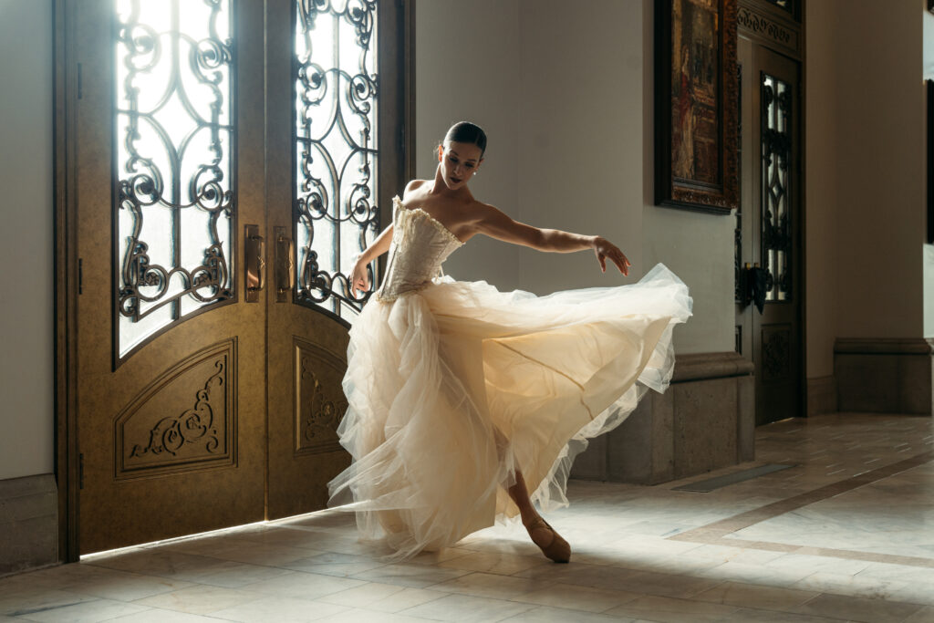 A ballerina elegantly dances in a sunlit hallway, wearing a flowing gown. Suitable for Ballet Idaho gala context.